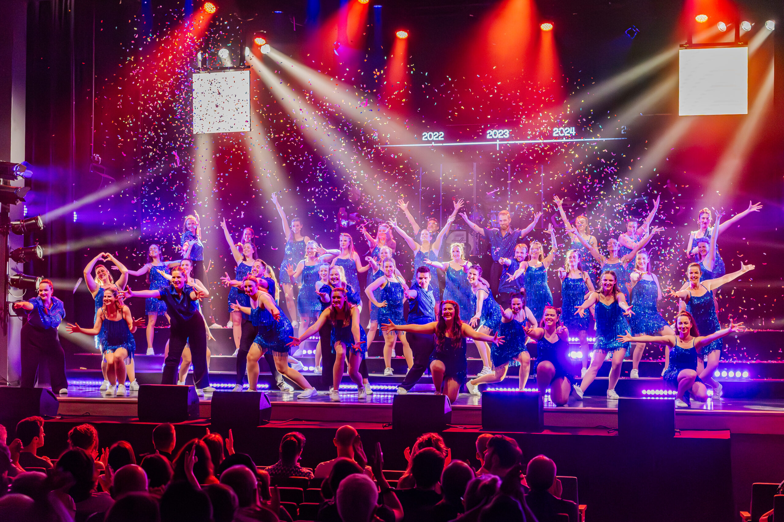 Koorleden dansen en zingen op het podium terwijl er confetti afgevuurd wordt